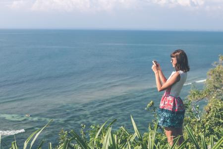 Woman Standing White and Blue Floral Dress Holding Smartphone in Grass Area