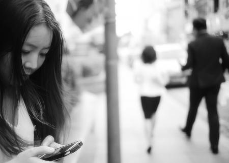 Woman Using Smartphone at Sidewalk Near Man and Woman Walking Away from Her