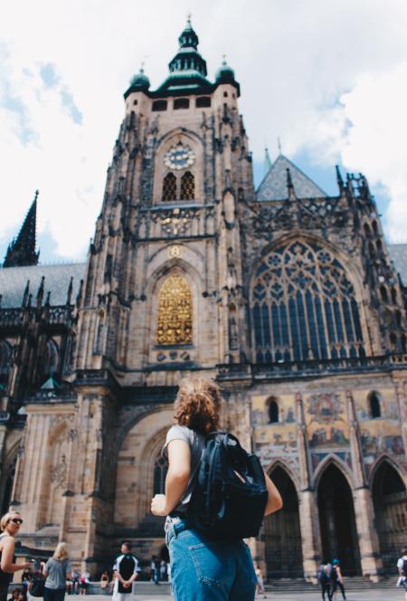 Woman Wearing Backpack And Grey Shirt Near Brown Church