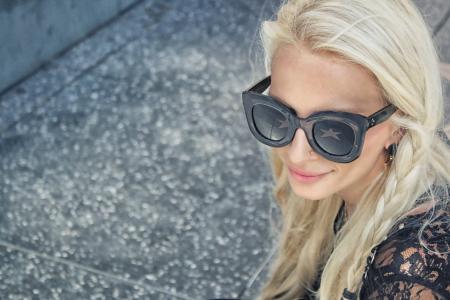 Woman Wearing Black Framed Wayfarer Style Sunglasses and Black Floral Top Near Gray Concrete Pavement