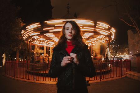 Woman Wearing Black Leather Jacket and Red Turtle-neck Shirt Standing in Front of Carousel Ride