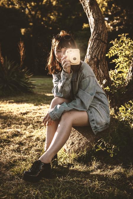 Woman Wearing Blue Denim Jacket Holding Pink Instant Camera Sitting on Soil
