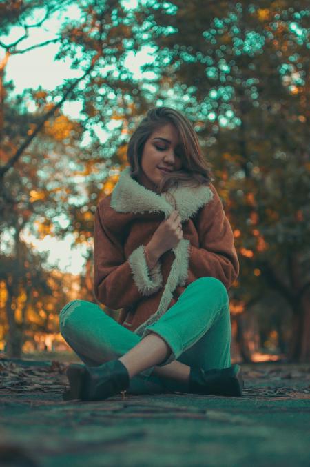 Woman Wearing Brown-and-white Coat and Teal Denim Jeans Sitting on Road Surface