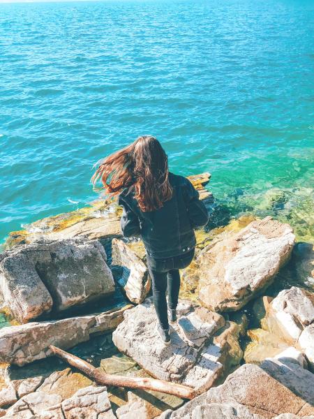 Woman Wearing Denim Jacket Standing on Rock Near Body of Water