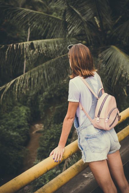 Woman Wearing Dungaree Shorts Stands Near a Yellow Metal Rail Overlook a River Belo With Coconut Trees at Daytime