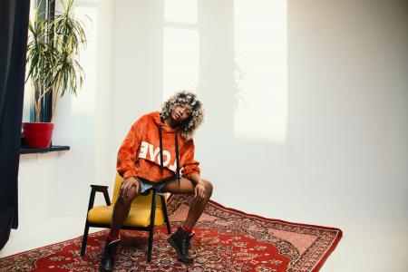 Woman Wearing Orange Pullover Hoodie Sitting on Chair's Arm