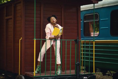 Woman Wearing Pink Blazer, Pants and Green Heeled Shoes Holding Yellow Covered Book