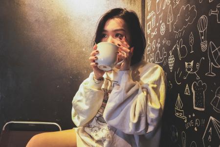 Woman Wearing White over Shirt Holding White Ceramic Mug Beside Black Printed Wall