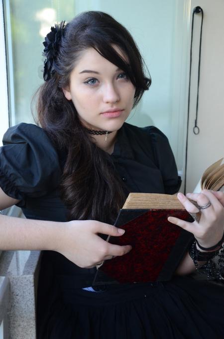 Woman With Black Hair and Wearing Black Cap Sleeve Dress Holding Book With Two Hands