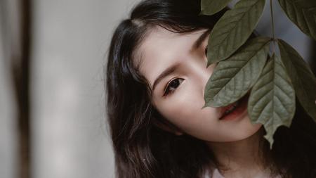 Woman With Black Hair Peeking Through Green Leaves