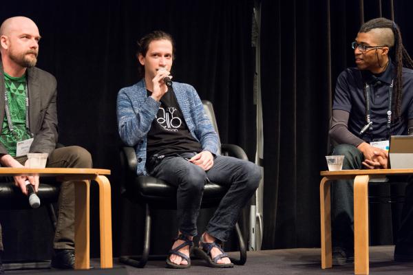 Aaron Lemke (Unello Design) discussing at indie dev panel at SVVR (full body view looking forward at audience with Denny Unger of Cloudhead Games on left and Cymatic Bruce on right)