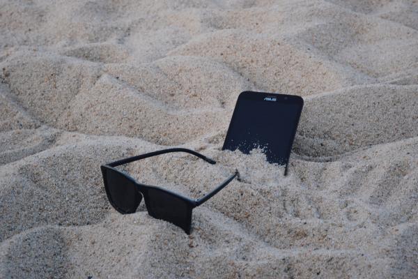 Black Wayfarer-style Sunglasses Beside Black Asus Android Smartphone on Brown Sand