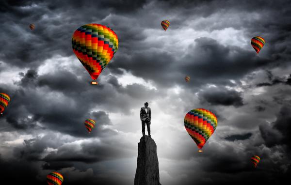 Businessman on the summit surrounded by hot air balloons