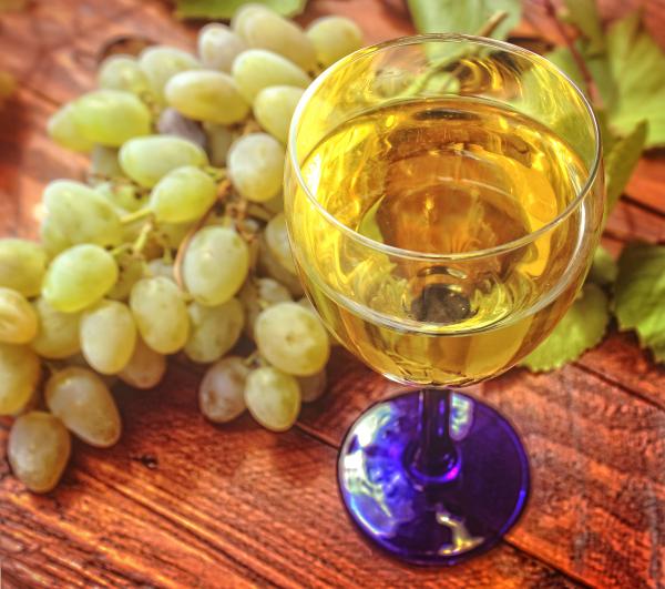 Glass of white wine and a bunch of grapes in the background