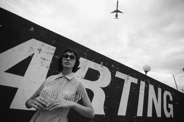Grayscale Photo of Woman Standing Beside Wall