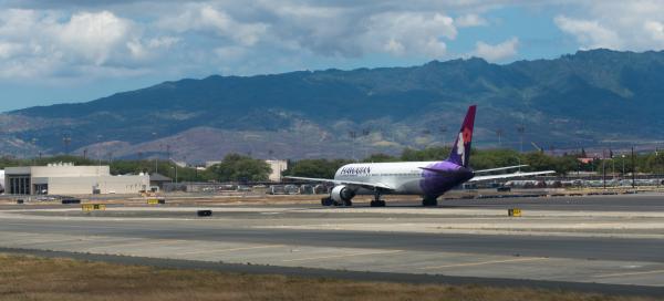 Hawaiian Airline plane on tarmac at Honolulu International Airport in front of hills