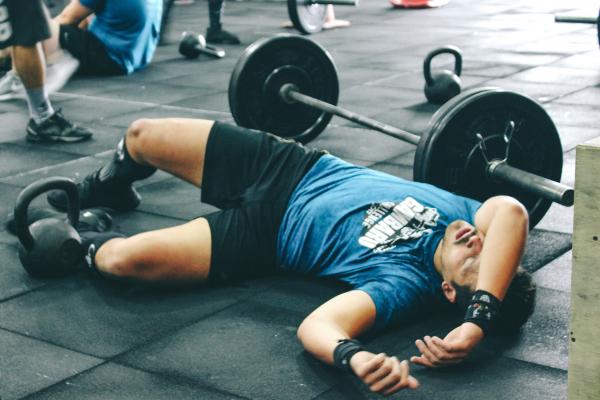 Man Lying on Rubber Mat Near Barbell Inside the Gym