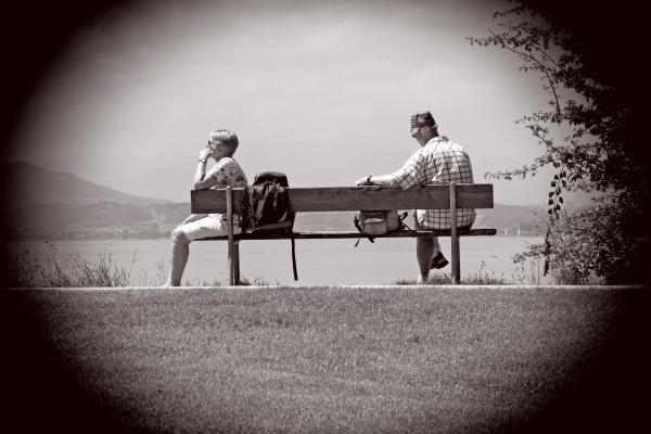 Man Sitting on Other Edge of Bench Parallel to Woman With Bags in Between Them