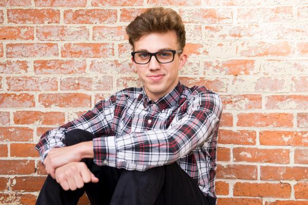 Man Wearing Plaid Dress Shirt And Black Pants Sitting Near Brown Brick Wall