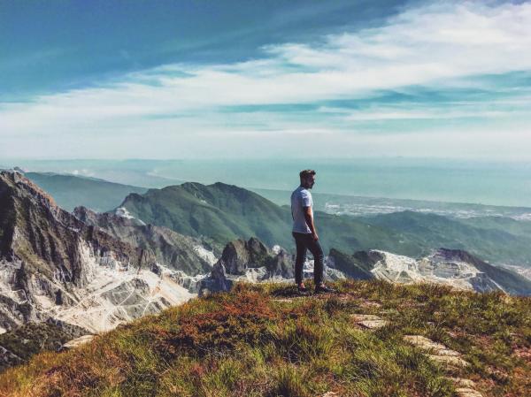 Man Wearing White T-shirt Standing on Mountain Under Blue Cloudy Sky