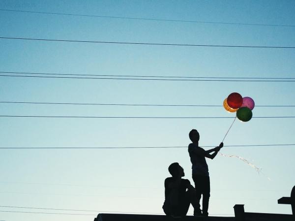 Men Holding Red Pink and Yellow Balloon Under Blue Sky during Daytime