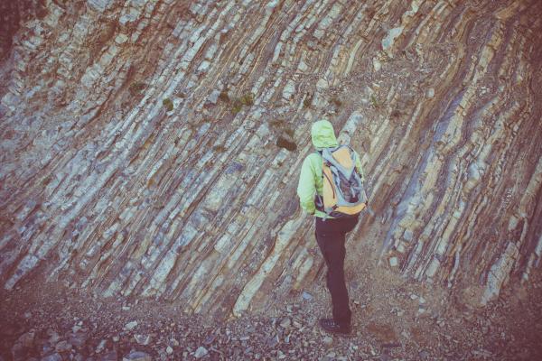Person in Green Hoodie and Black Pants Walking Near Gray Rock