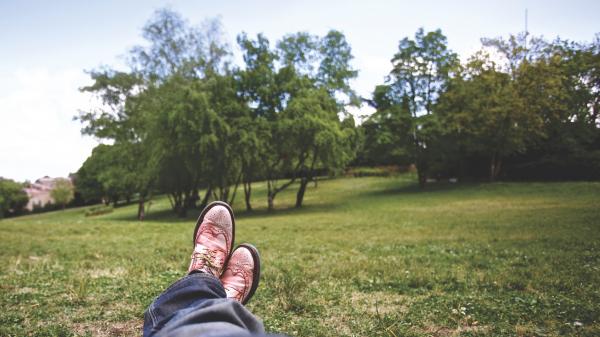 Person Lying on Grass Field Near Trees Under White Clouds during Daytime