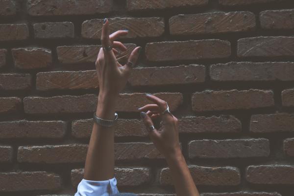 Person Raising Its Two Hand Beside Brown Brick Wall