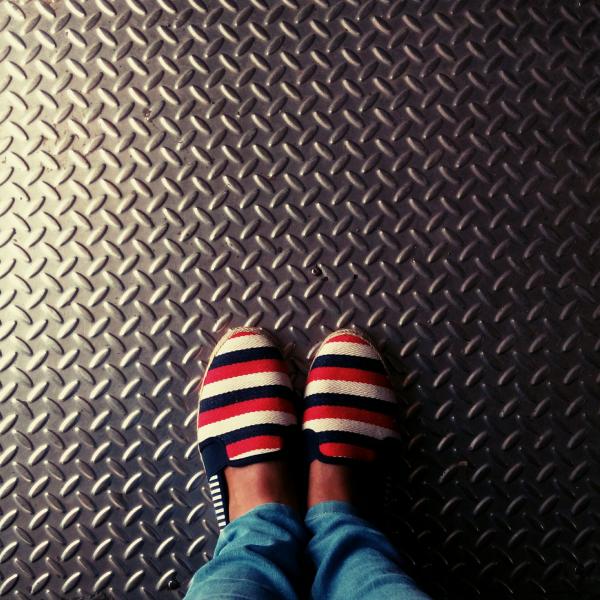 Person Wearing Red-and-multicolored Slip-on Shoes Standing on Gray Metallic Diamond Plate