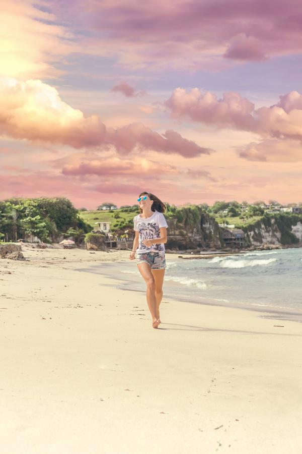 Smiling Woman Walking Barefood on Seashore Near Houses