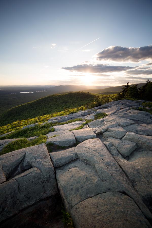Sunset over the Horizon Surrounded by Green Mountains on a Clear Blue Sky