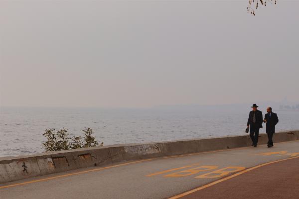Two Person Walking on a Concrete Road Beside Body of Water