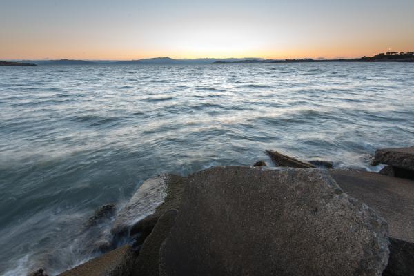 Waves crashing on rocks at bay shore at sunset