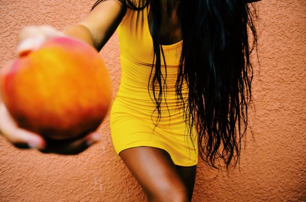 Woman Holding Round Fruit While Leaning on Orange Wall