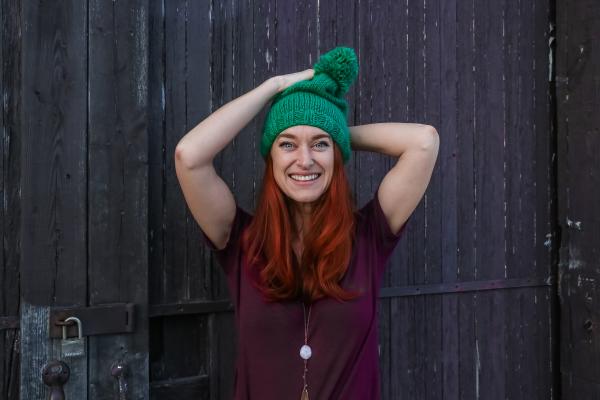 Woman in Green Bobble Cap and Purple T-shirt Posing Near Black Wooden Fence