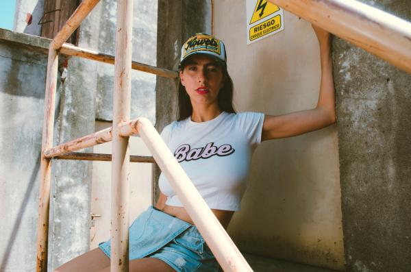 Woman in White Crew-neck Babe Printed Cap-sleeved Crop-top With Blue Denim Miniskirt Sitting Near Brown Metal Door