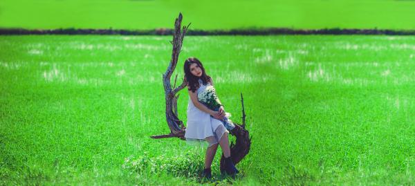 Woman in White Sleeveless Mini Dress Holding White Petaled Bouquet Sitting on Gray Tree Branch at Daytime