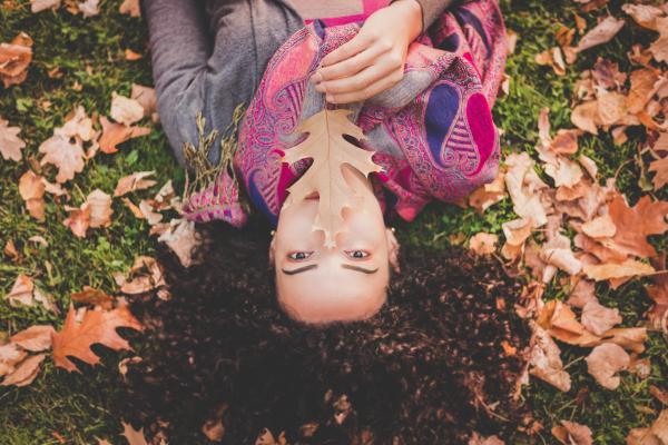 Woman Lying Down On Green Grass Field Holding Brown Leaf