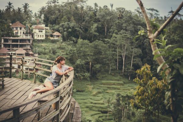 Woman Sits On Bench Overlooking Tall Trees At Daytime