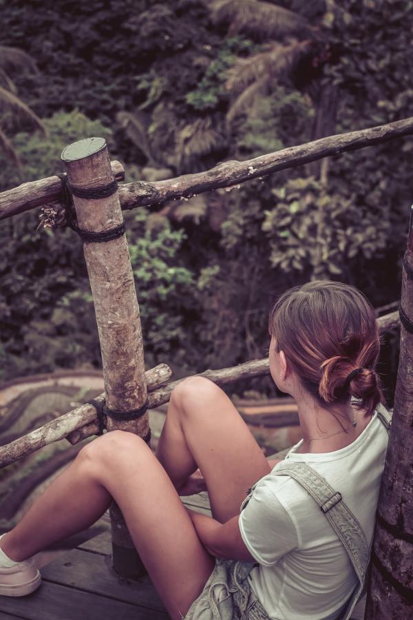 Woman Wearing White Shirt and Shortalls Sitting on Wooden Terrace