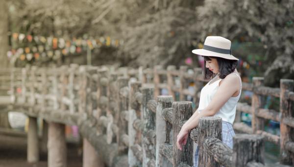 Woman Wearing White Tank Top and White Hat Standing on a Boardwalk